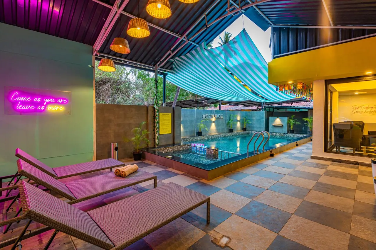 A covered pool courtyard has a small swimming pool, loungers, potted plants and striped shade canopies.