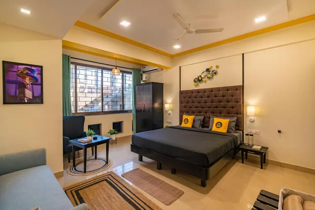 A bright bedroom contains a double bed, seating area, wardrobe, ceiling fan and air-conditioning unit.