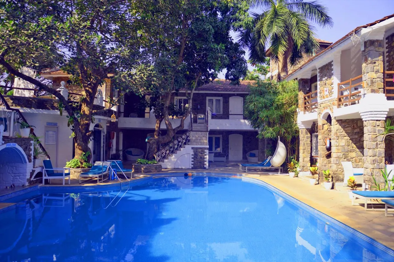 A large swimming pool is surrounded by sun loungers and tropical planting in a stone-and-plaster courtyard.