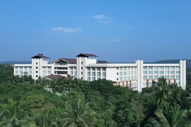 A white resort building stands among tropical greenery beneath a blue sky.