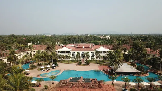 A large resort pool complex and colonial-style buildings are surrounded by palm trees and landscaped grounds.