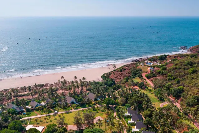 An elevated view shows a sandy beach, blue sea, palm trees, and landscaped resort grounds.
