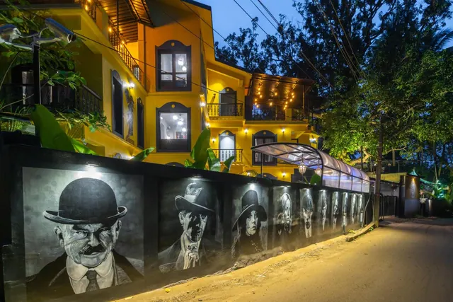 A brightly lit yellow hotel building with balconies and a painted portrait mural along the street-facing wall.