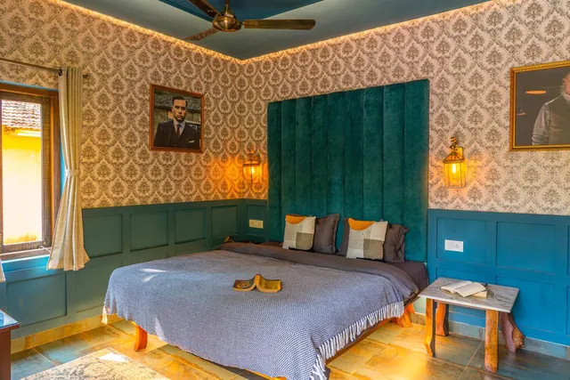 A furnished bedroom has a double bed, patterned walls, a ceiling fan and framed portraits.