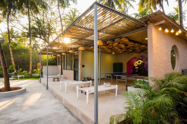 A covered outdoor recreation area contains a table tennis table, woven seating and tropical plants.