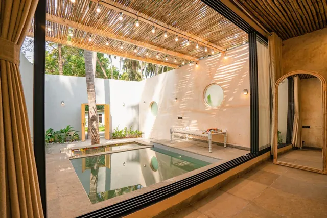 A small pool occupies a tropical courtyard beside an open-sided room with a bamboo canopy.